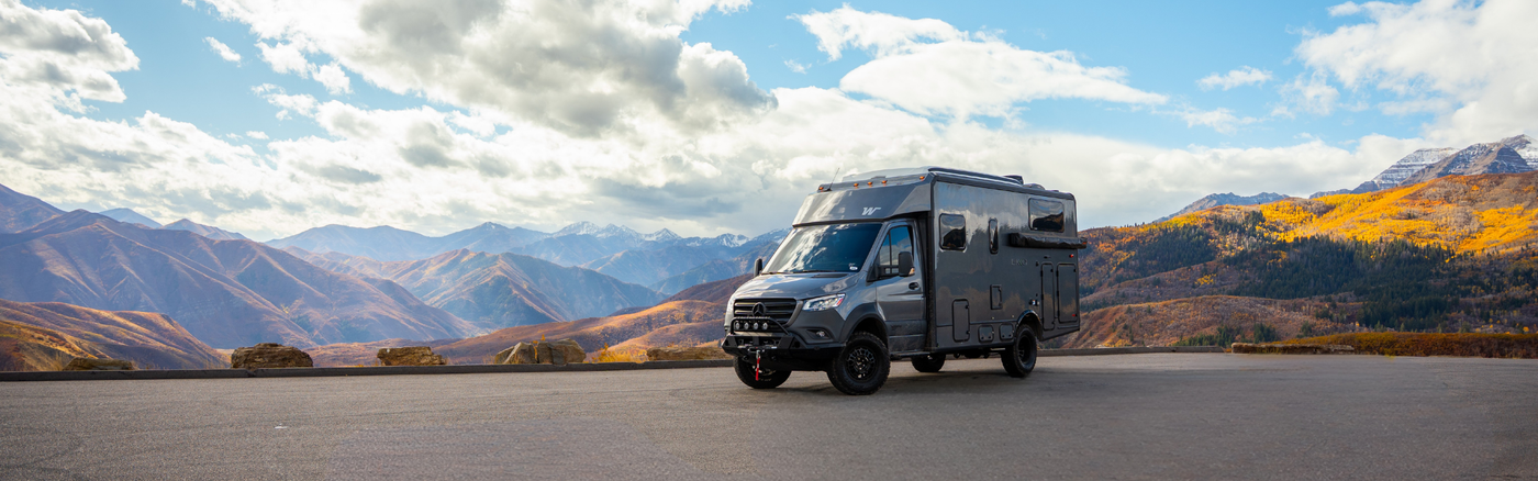 Camper Van parked at a lookout view point with snow dusted mountains and fall foliage in the background.